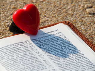 
Open bible page 1 Corinthians 13:4 Love is patient. And red heart on beach sand. God is love ,...
