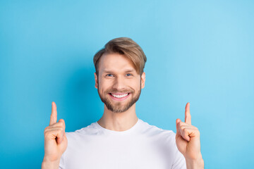 Photo of friendly man toothy smile look camera direct fingers up empty space isolated on blue color background