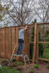 A white, middle-aged gay man builds a wooden fence in his back yard.