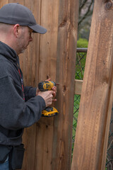 A white, middle-aged gay man builds a wooden fence in his back yard.