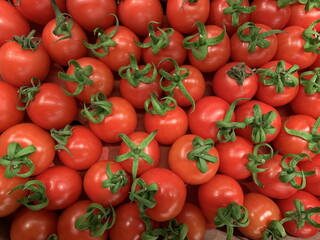 Red small cherry tomatoes, close-up. Background texture: ripe tomatoes with green twigs. Juicy vegetables, bright red.