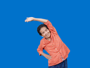 Portrait Of active senior old woman warming stretching exercising isolated on blue background. Happy mature or elderly lady smiling and enjoying doing sport. Fitness and healthy lifestyle concept.