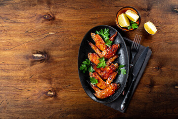  Baked chicken wings with sesame seeds, parsley and lemon on a black plate top view, free space for text