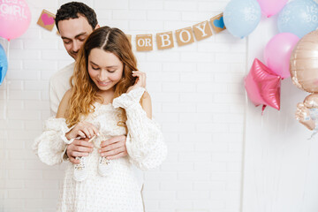 Young happy couple posing with baby shoes during gender reveal party
