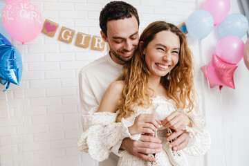 Young happy couple posing with baby shoes during gender reveal party