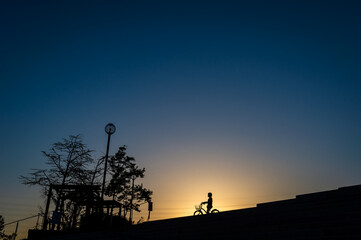 Fototapeta na wymiar 夕暮れの高台のシルエット、自転車の女の子、宝塚市北公園、4月19日、日本