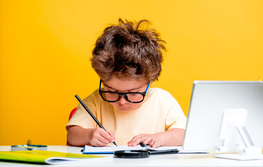 Naklejka na ściany i meble Portrait of smart school child boy at home making homework with tablet computer. Little kid in glasses with pencil writing or drawing. Elementary school and education for kindergarten kids