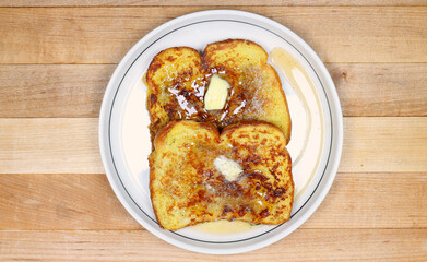 French Toast, two slices on a small plate, melted butter, syrup and cinnamon, overhead, straight down, butcher block background.