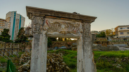 DURRES, ALBANIA: Exterior of ancient Roman amphitheater with surrounding buildings in the city of...