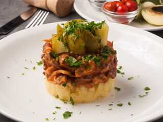 beef stroganoff with mashed potatoes and pickles on a white plate