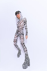 Fashion androgenic blonde model in freak stylish zebra print clothes and boots posing in a white studio. Accessory trend leather cap