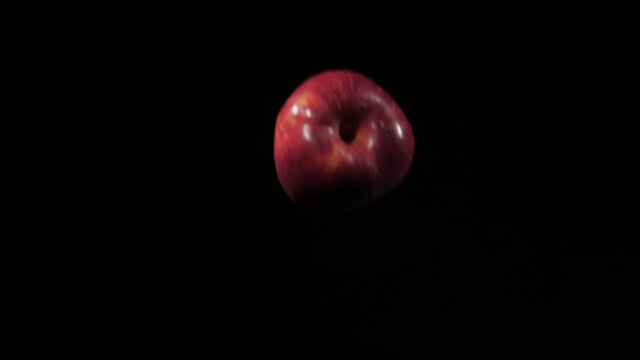 Close up on a group of three fresh red apples fly up and spinning on a black background in slow motion shot