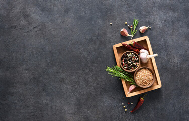 A set of spices: chili, mustard, rosemary, garlic in a wooden box on a black background. Layout.