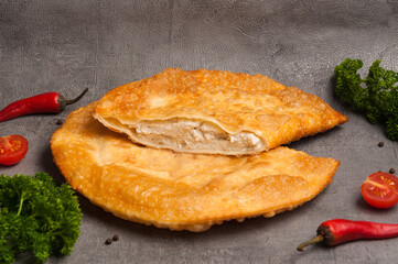 cheburek with chicken on a gray background decorated with herbs and vegetables