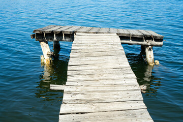 Fototapeta premium An old empty wooden deck on a lake. Fishing pier made with weathered woods.