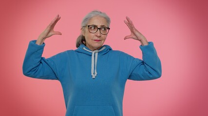 Elderly granny woman showing bla-bla-bla nonsense gesture with hands and rolling eyes, gossips, empty promises, blah concept. Lier. Senior old grandmother on pink background. People lifestyle emotions