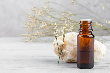 Glass dark cosmetic bottle, a stone and a sprig of a flower against the background of a bouquet of dried flowers, front view. Aromatherapy, massage oil, natural organic cosmetic, alternative medicine.