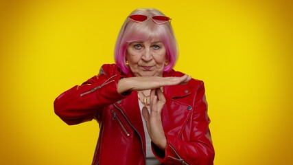 Tired serious upset mature old stylish rocker granny woman with pink hair showing time out gesture, limit or stop sign, no pressure, i need more time. Senior grandmother isolated on yellow background