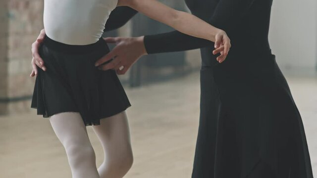 Tilting-up up shot of little hard-working girl learning to dance ballet with help of professional female trainer practicing ballet poses in dance studio