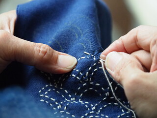 Close up needle in woman's hands sewing running stitch in blue fabric. Traditional Japanese sewing...