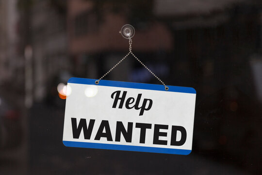 Close-up on a blue open sign in the window of a shop displaying the message "Help wanted"..