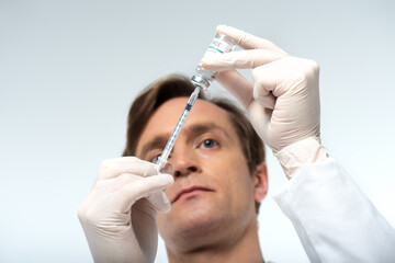 Low angle view of doctor piking up vaccine in syringe isolated on grey