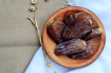 Dates (Phoenix dactylifera) on a wooden bowl on a white and brown cloth background. food for breaking the fast during Ramadan for Muslims. selective focus