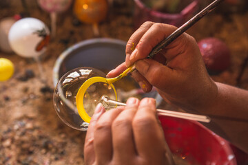 Craftsman painting Christmas spheres in his workshop in different colors, using acrylic paint, diamond paint to give texture and different figures.