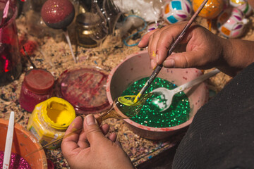 Craftsman painting Christmas spheres in his workshop in different colors, using acrylic paint, diamond paint to give texture and different figures.