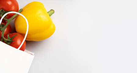 White paper bag with tomatoes and yellow pepper on gray background, place for text,top view