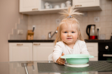 Cute little blonde girl eats in the kitchen of the house