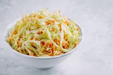 Traditional coleslaw salad with fresh sliced carrots and cabbage in a white bowl