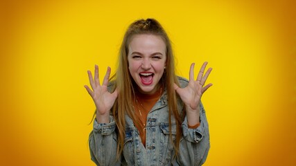 Little bit crazy. Teen stylish girl in denim jacket demonstrating tongue out, fooling around, making silly faces, madness. Young woman posing isolated on yellow studio wall background. Slow motion