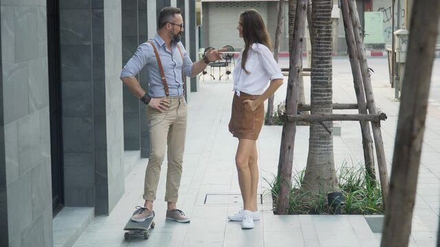 Young hipster couple riding skateboards and talking together  on street in urban city
