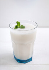 Glass of lassi Indian traditional, milky, fermented drink with mint on a light background