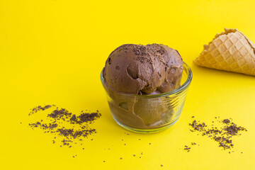 Close-up on chocolate ice cream in a glass bowl on the yellow  background. Copy space.