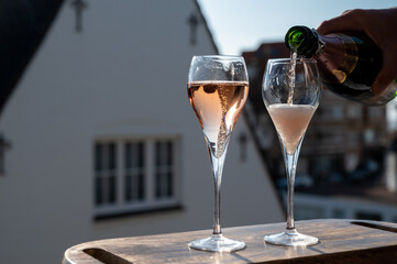 Pouring of rose champagne sparkling wine in flute glasses on outdoor terrace in France