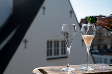 Pouring of rose champagne sparkling wine in flute glasses on outdoor terrace in France