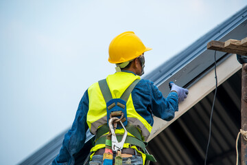Professional and qualified roofer in protective uniform wear use electric drill to install the metal sheet on the new roof of new modern building construction.