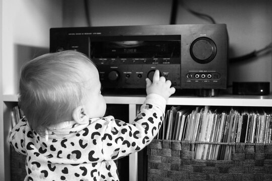 10 month old toddler pulling up to reach stereo; using hand to turn knobs.  Record collection nearby