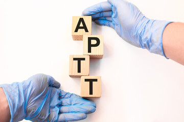 A doctor wearing gloves holds wooden cubes with the inscription APTT, medical concept