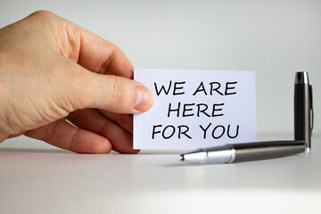 Help and support symbol. White paper with words 'we are here for you' in businessman hand, metalic pen. Beautiful white background. Business, help and support concept. Copy space.