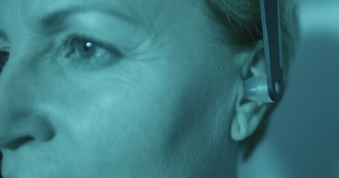 Close-up face of a female patient and inside of her ear is putting a detail for having scanning of her head inside of Cephalometric X-ray unit.
