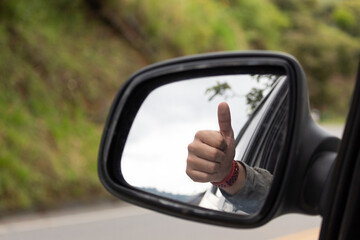 hand and finger up in rear-view mirror of a car