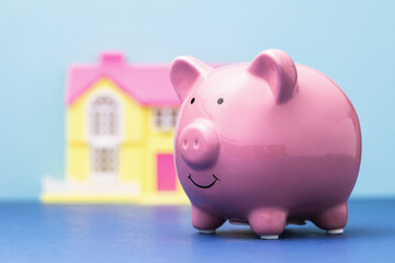 Ceramic piggy bank and a toy house on a colored background, the cost of housing