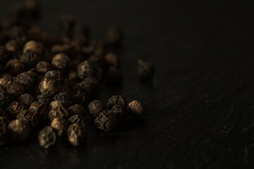 Close up of group of dried peppercorns in the left center on slate plate
