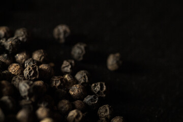 Close up of group of dried peppercorns in lower left corner on slate plate