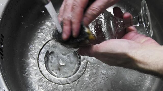 A man washes a glass goblet with a sponge. Home life. Live video.