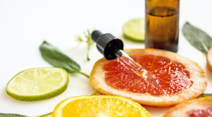 Natural cosmetics with vitamin C, a bottle with a cosmetic product with citrus essential oil on the background of plastics of lemons, oranges, grapefruit. Copy space. Citrus skin whitening concept