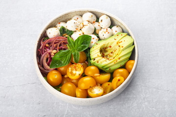 caprese salad with mozzarella, yellow cherry tomatoes, avocado, red onion, basil on a gray background